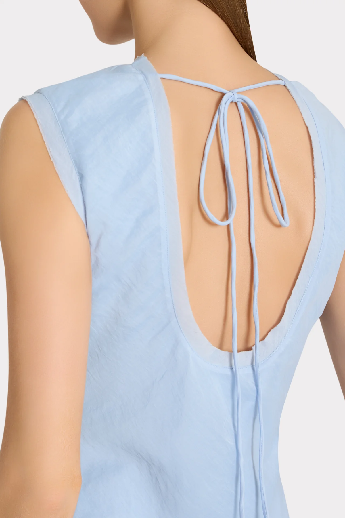 Light blue sleeveless top with open back and tie details on a neutral background