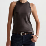 Woman wearing a brown sleeveless top and dark jeans on a white background