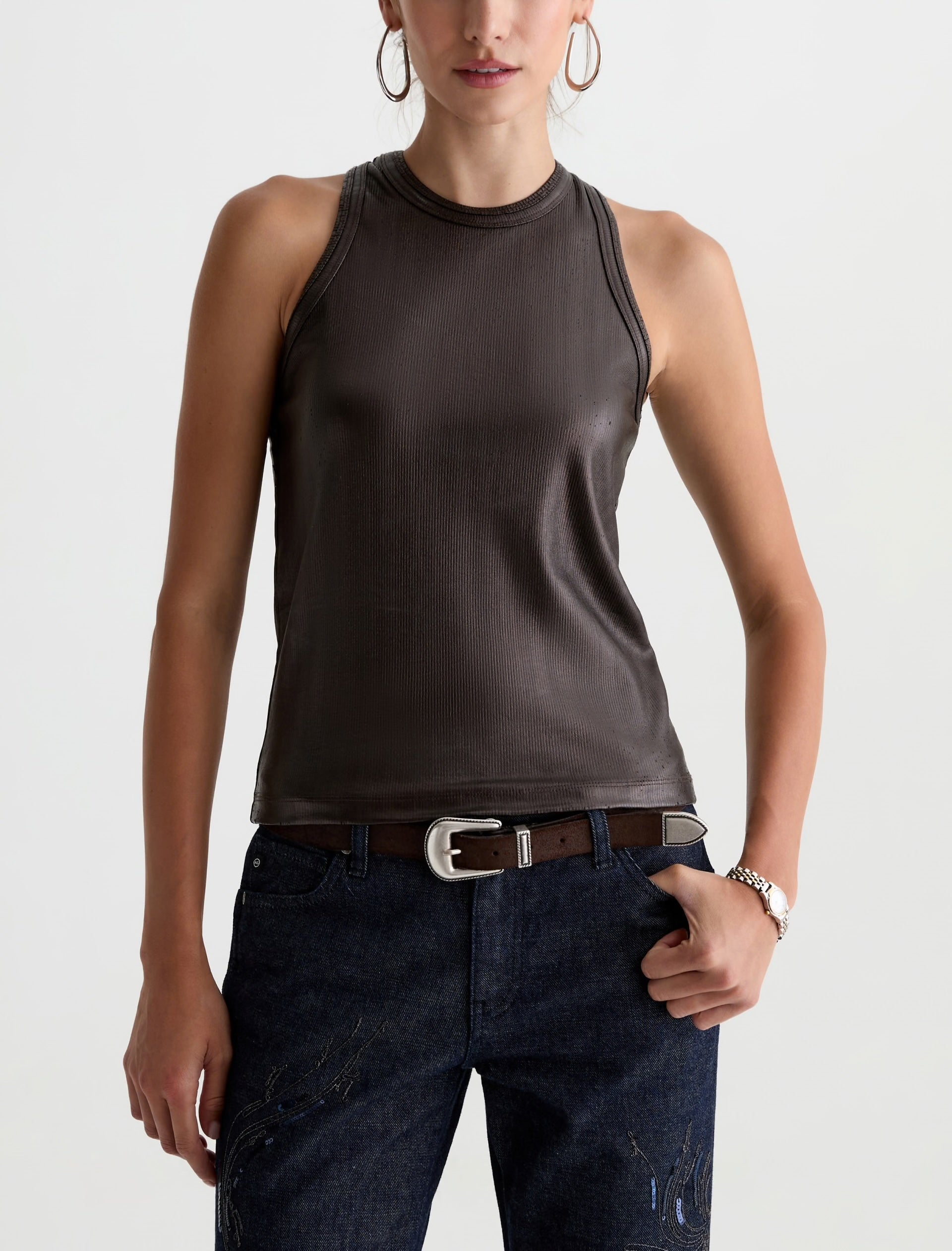 Woman wearing a brown sleeveless top and dark jeans on a white background