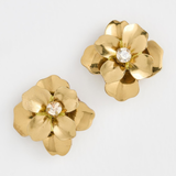 A pair of gold flower-shaped earrings with a clear rhinestone center, displayed on a clean white background.