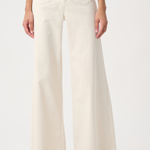 A model wearing a pair of off-white wide-leg jeans with gold-tone hardware on the front pockets, paired with beige flats, against a plain white studio background.