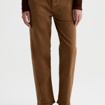A person wearing brown straight-leg pants with a dark brown long-sleeve top and black ankle boots, shown from the waist down against a light gray studio background.