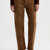 A person wearing brown straight-leg pants with a dark brown long-sleeve top and black ankle boots, shown from the waist down against a light gray studio background.