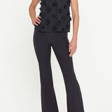 Woman wearing a black sleeveless top with floral embellishments and black pants on a white background