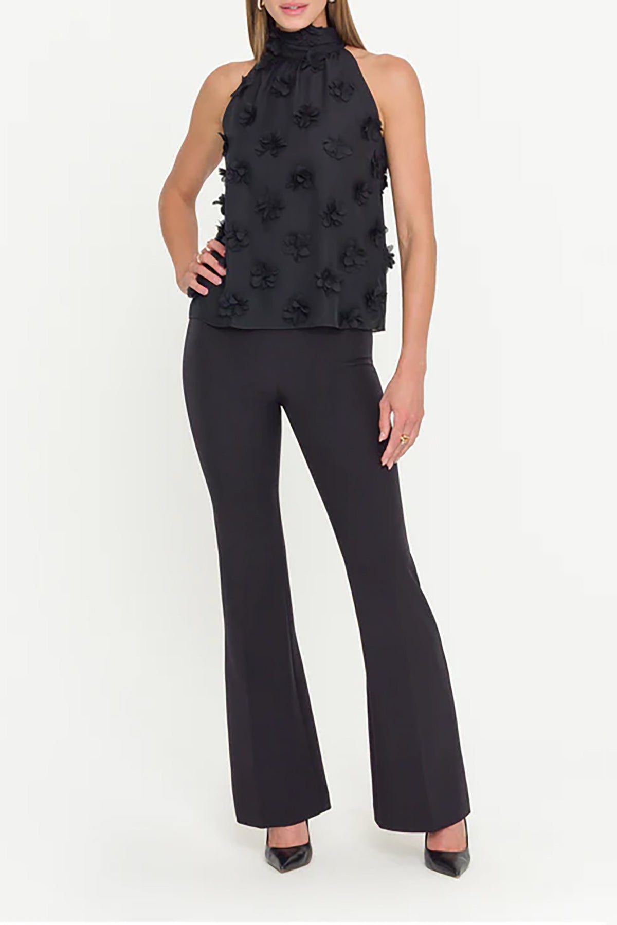 Woman wearing a black sleeveless top with floral embellishments and black pants on a white background