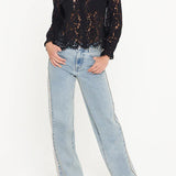 Woman wearing a black lace blouse and light blue jeans on a white background