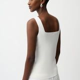 Woman wearing a white sleeveless top and white pants on a plain background