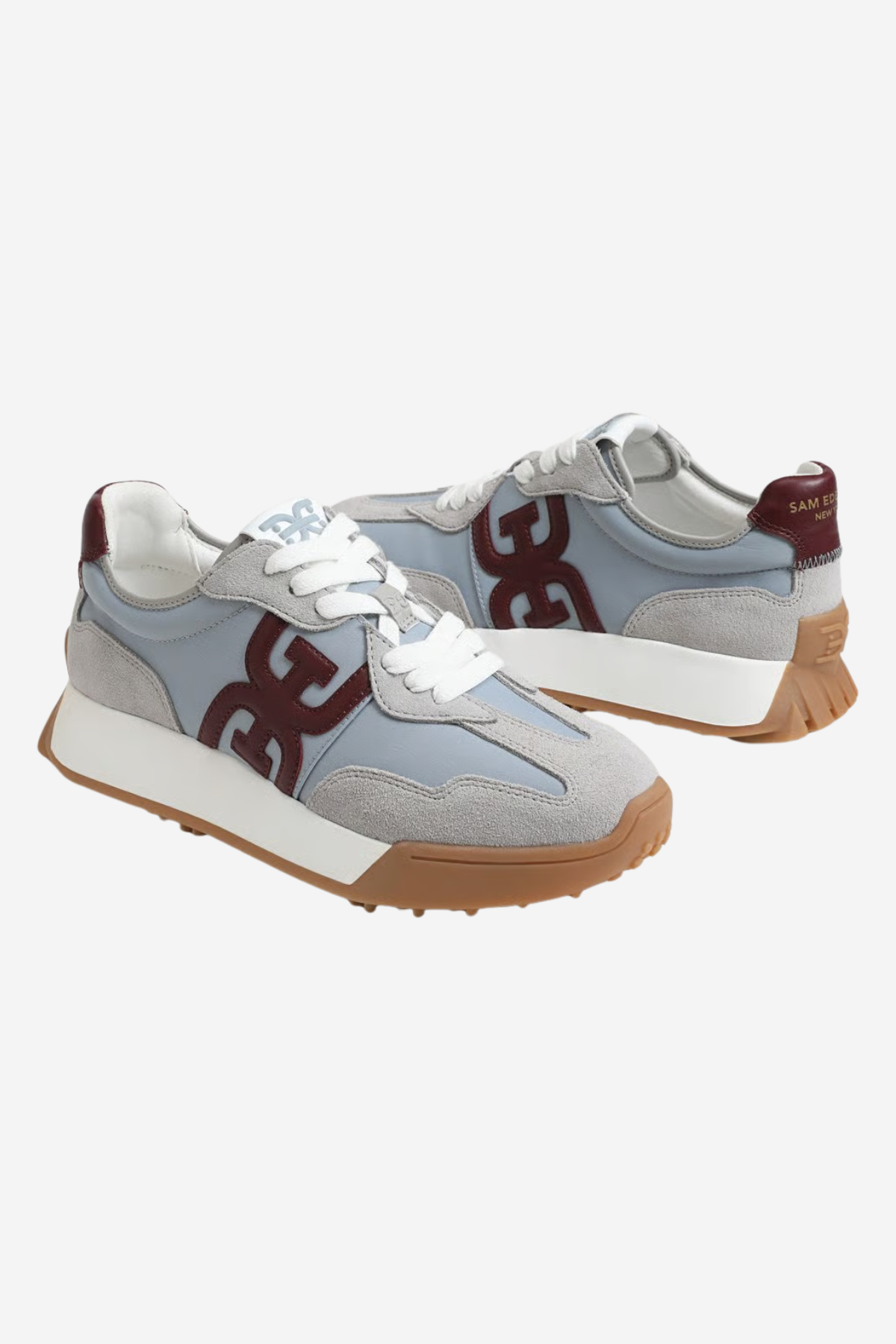 A pair of low-top sneakers in light blue suede and mesh, featuring a large dark burgundy 'G' logo on the side, white laces, a white midsole, and a brown gum outsole, shown against a light gray background.