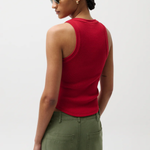 Woman wearing a red sleeveless top and green pants against a white background
