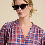 Woman wearing sunglasses and a plaid shirt against a beige background