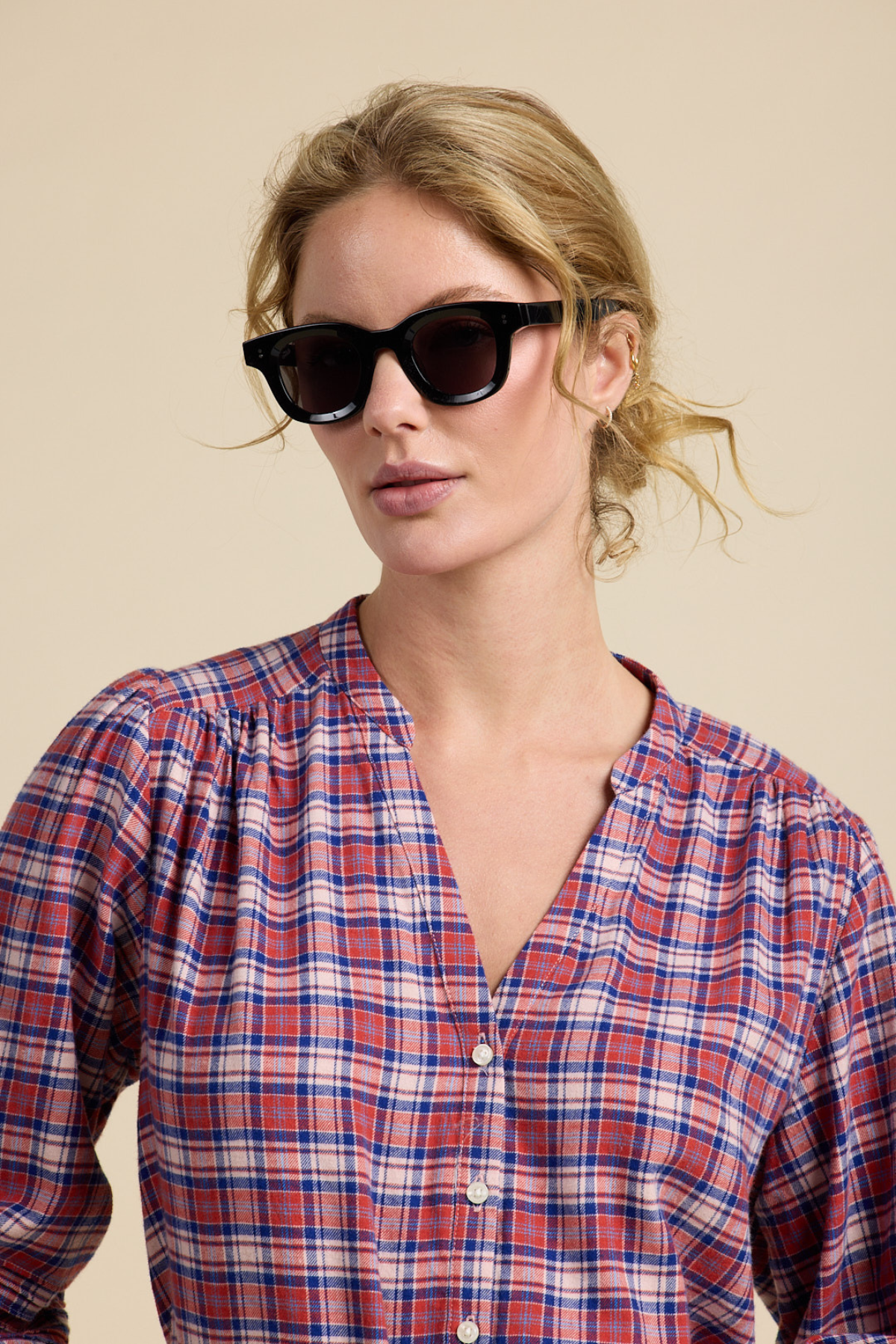Woman wearing sunglasses and a plaid shirt against a beige background