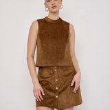 A woman modeling a brown suede-like sleeveless top and matching mini skirt with front buttons, photographed against a plain light gray studio background.