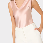 Woman wearing a pink satin top and white shorts on a light gray background