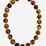 A beaded necklace made of polished round amber-brown glass beads with a small gold clasp, shown on a plain light gray background.