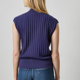 A woman shown from the back wearing a sleeveless, ribbed knit top in a deep purple shade, paired with blue jeans, against a light gray studio background.