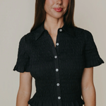 Model wearing a dark short-sleeve collared blouse with a relaxed fit, styled with a printed skirt against a neutral studio backdrop.