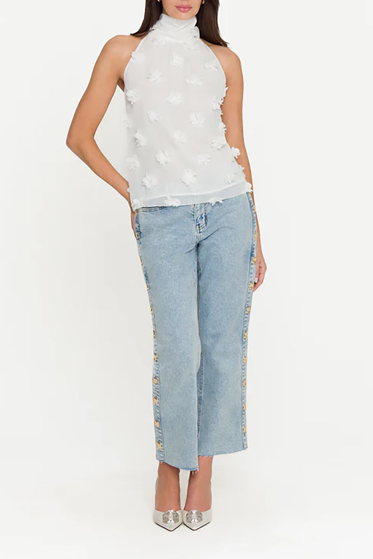 Woman wearing a white sleeveless top with floral details and light blue jeans on a white background