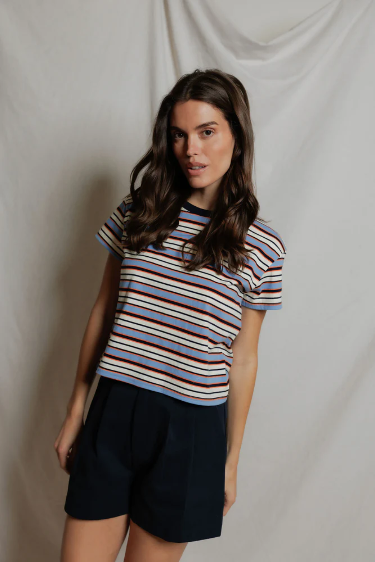 Woman wearing a striped shirt and black shorts against a plain background