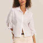 Woman wearing a white blouse with tied sleeves against a plain background