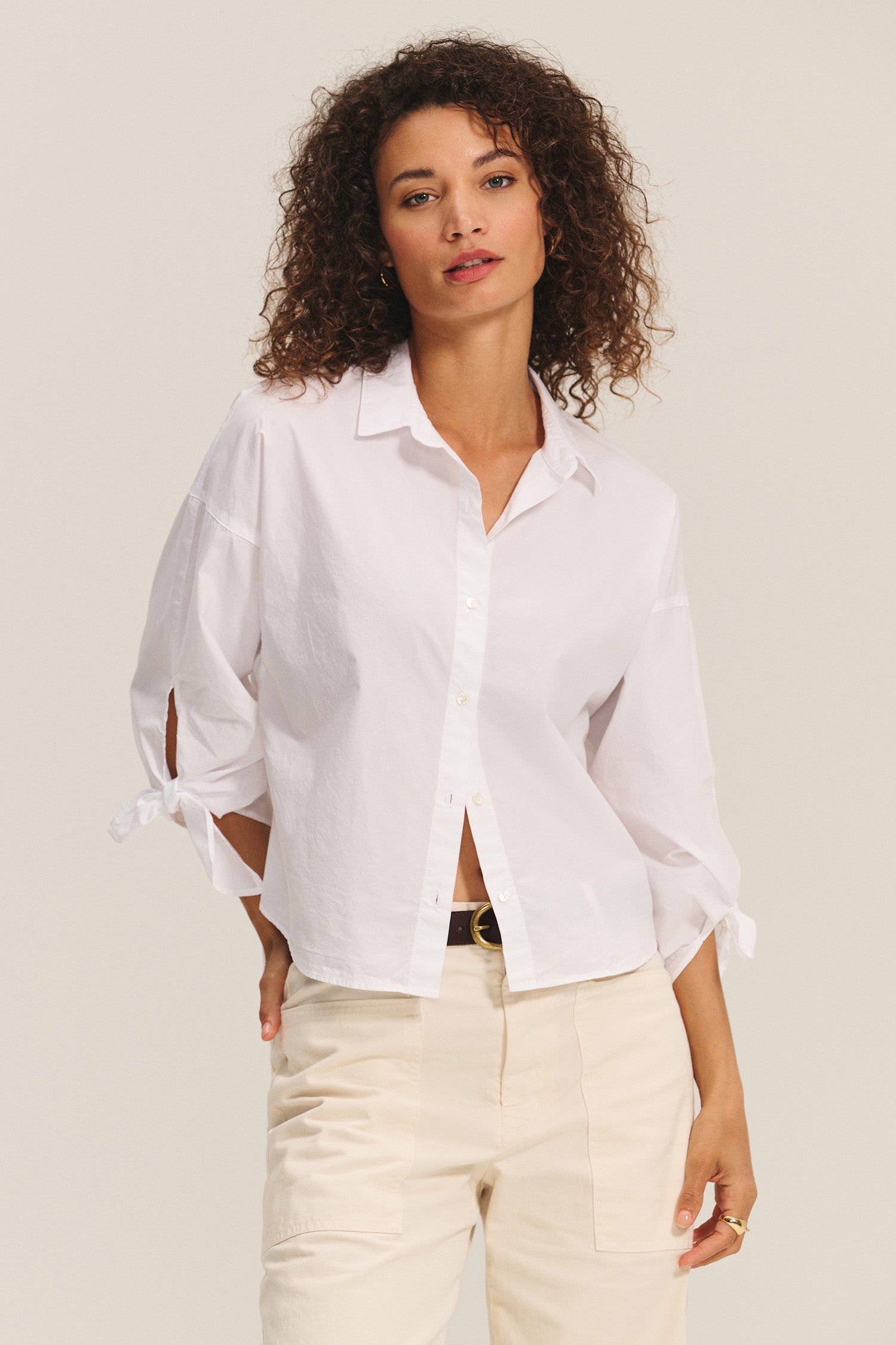 Woman wearing a white blouse with tied sleeves against a plain background