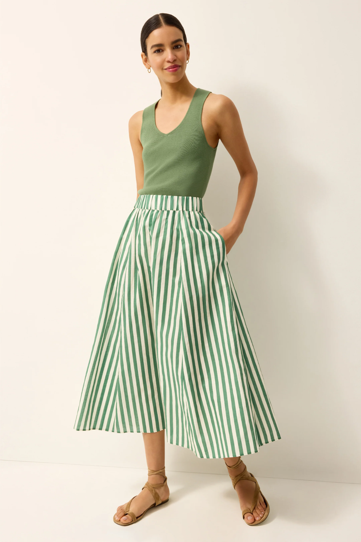 Woman wearing a green tank top and green and white striped skirt against a white background