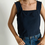 Woman wearing a navy blue sleeveless top and blue jeans against a white background