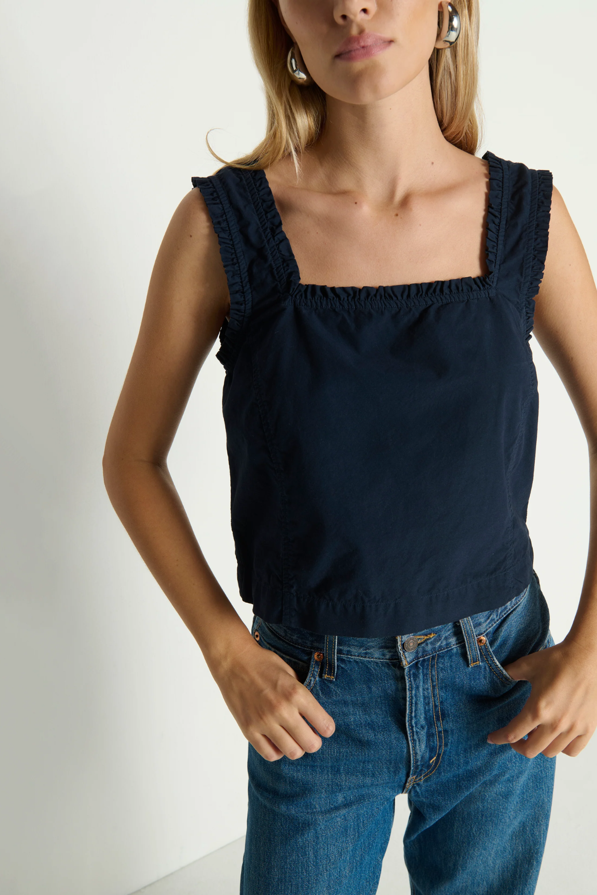 Woman wearing a navy blue sleeveless top and blue jeans against a white background