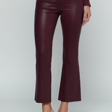 A model wearing high-waisted, cropped flared pants in a deep burgundy faux-leather material, paired with a matching long-sleeve top and dark brown heeled sandals, against a light gray studio background.