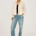 Woman wearing a cream jacket and light blue jeans on a white background