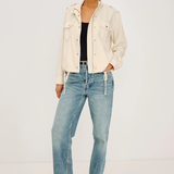 Woman wearing a cream jacket and light blue jeans on a white background