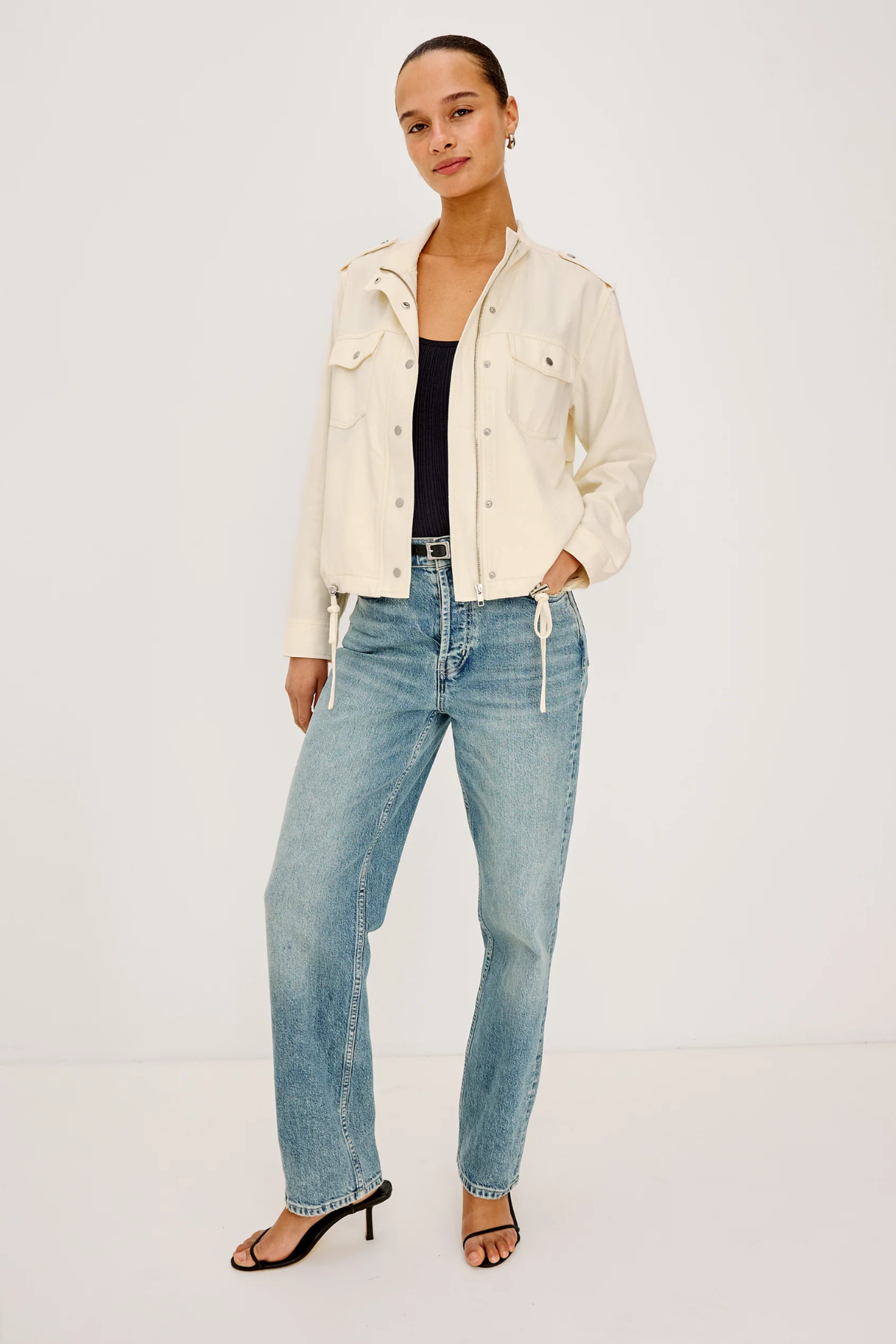Woman wearing a cream jacket and light blue jeans on a white background