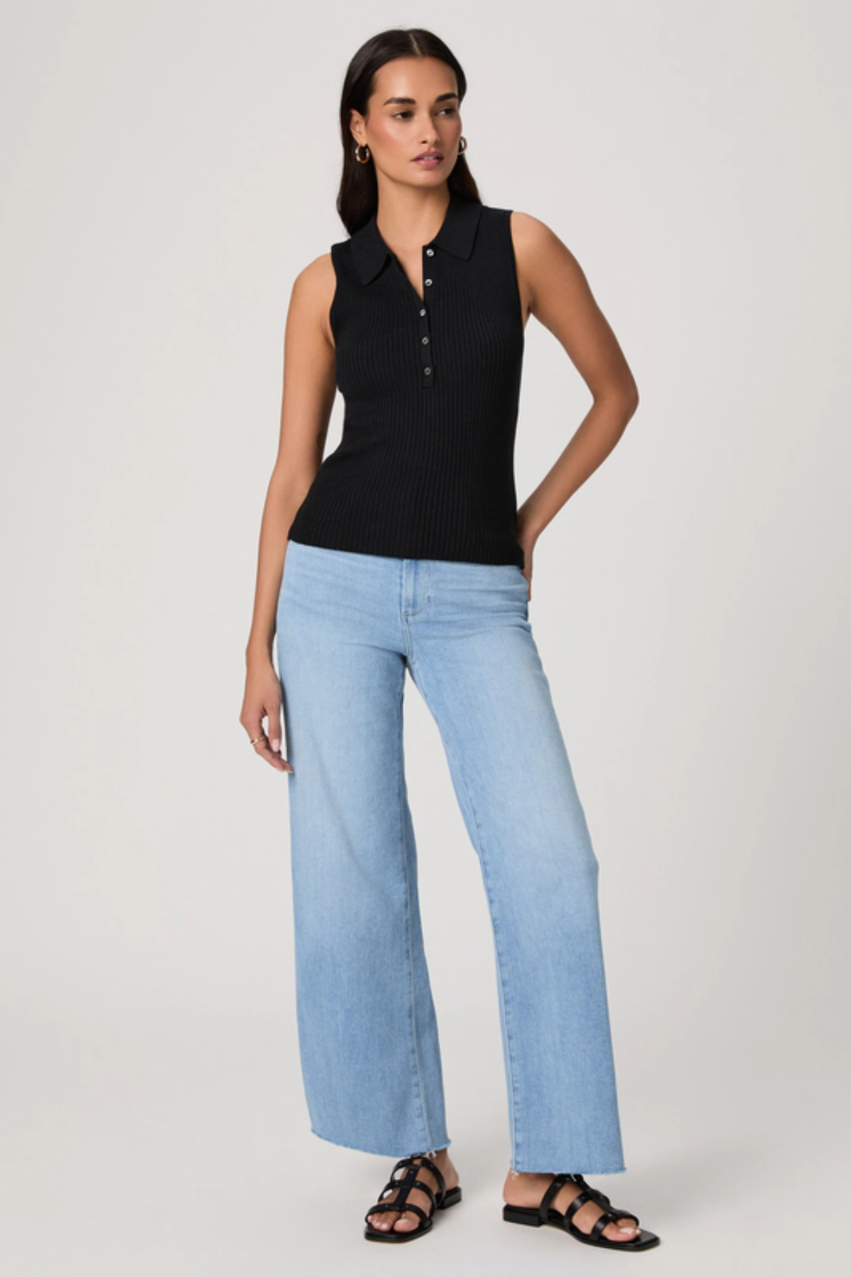 Woman wearing a black sleeveless polo shirt and light blue jeans on a white background