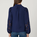 Navy blue blouse with lace sleeves back view by a person on a light gray background