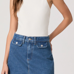 Person wearing a white tank top and blue denim skirt on a plain background