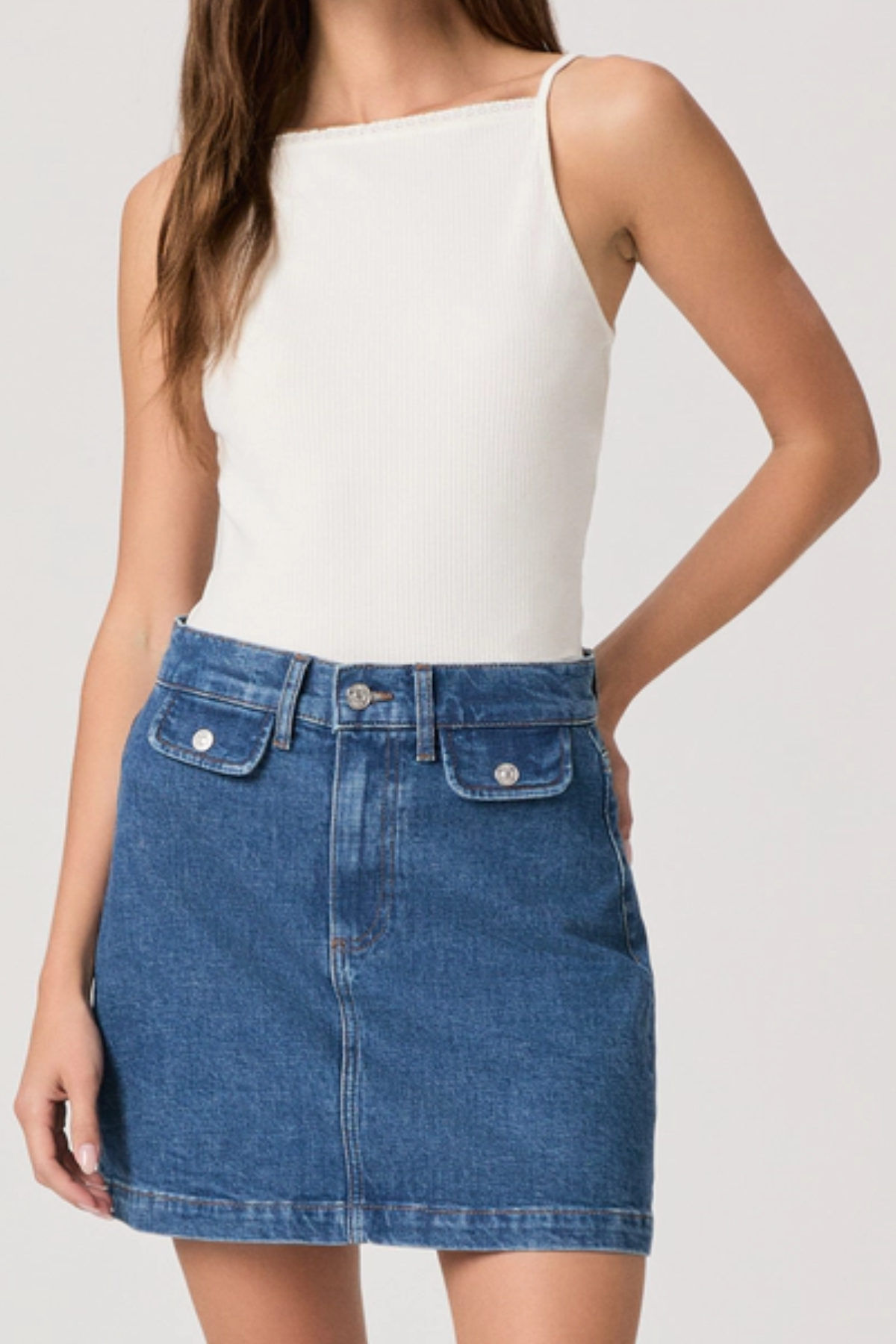 Person wearing a white tank top and blue denim skirt on a plain background