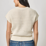 Woman wearing a cream ribbed sweater and blue jeans on a light gray background