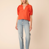 Woman wearing a bright orange top and light blue jeans on a beige background