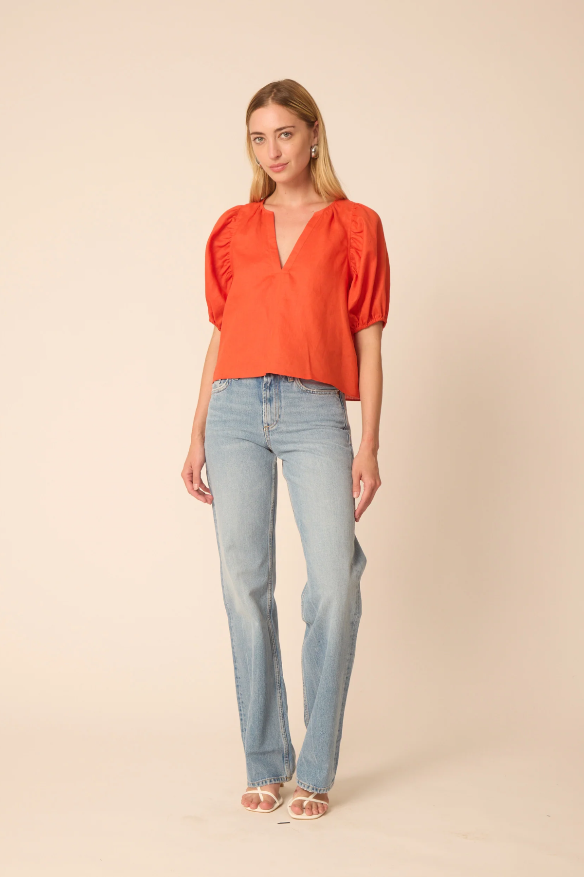 Woman wearing a bright orange top and light blue jeans on a beige background