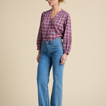 Woman wearing a plaid shirt, blue jeans, and brown shoes on a beige background