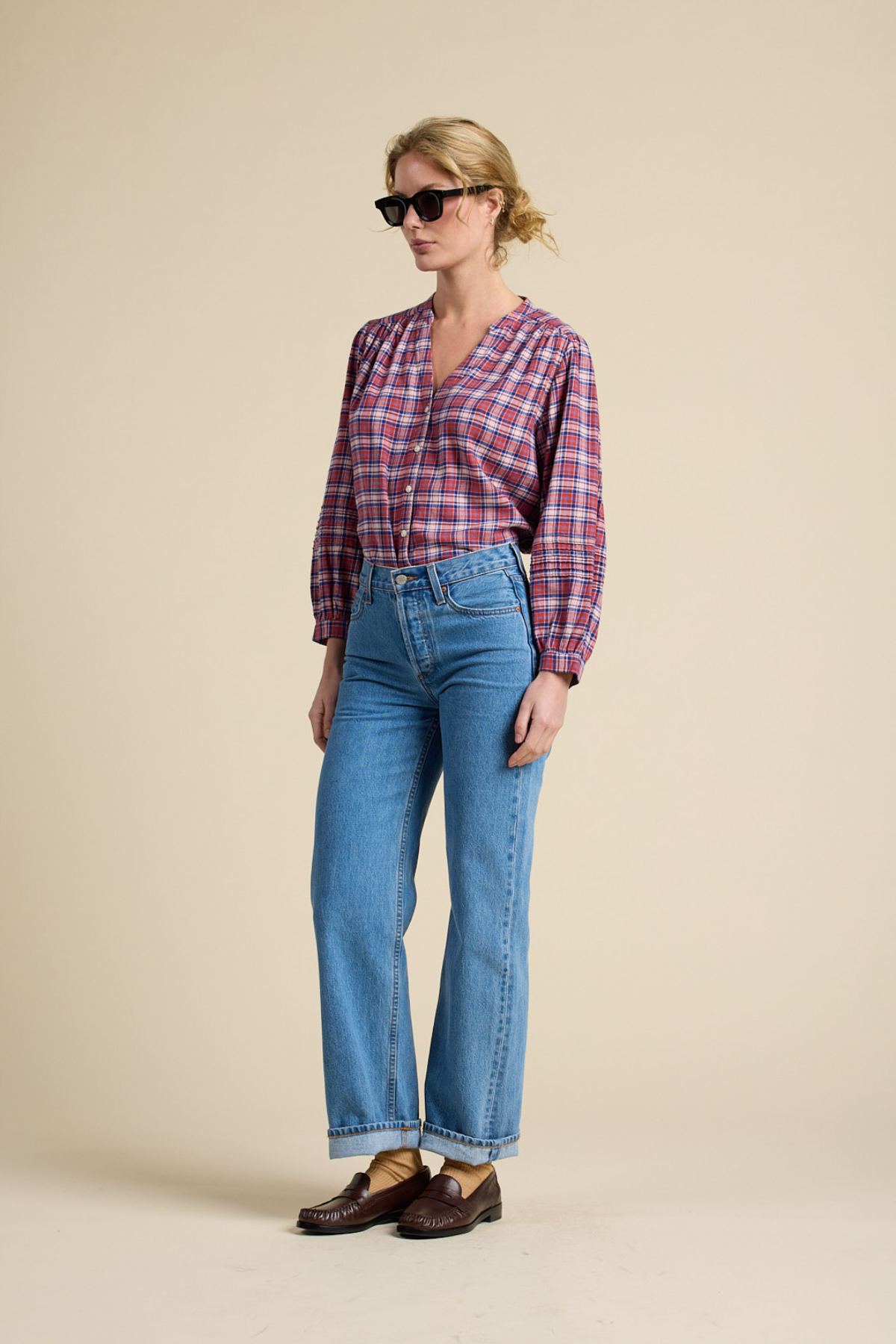 Woman wearing a plaid shirt, blue jeans, and brown shoes on a beige background