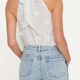 Woman wearing a white one-shoulder top with a bow and light blue jeans on a white background