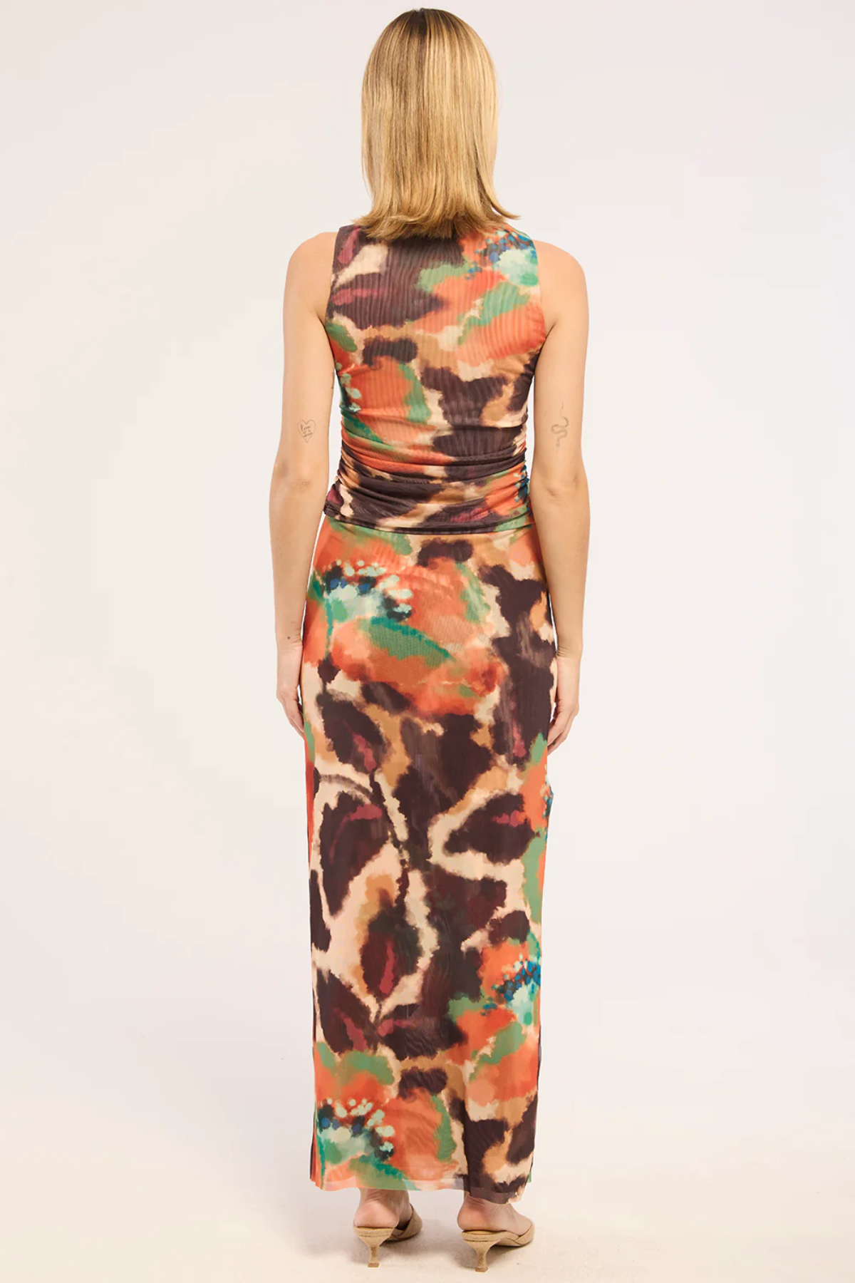Woman wearing a sleeveless, multicolored top and dress with a white background back view