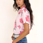 Woman wearing a pink floral blouse and blue jeans against a white background