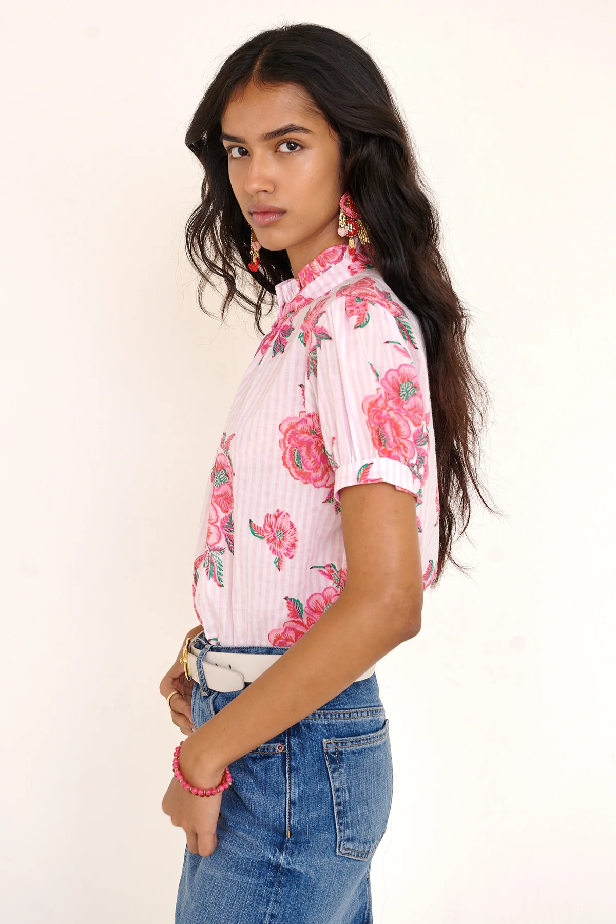 Woman wearing a pink floral blouse and blue jeans against a white background