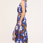 A woman modeling a sleeveless midi dress with a blue, brown, and white abstract pattern, shown in profile against a plain light background.