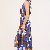 A woman modeling a sleeveless midi dress with a blue, brown, and white abstract pattern, shown in profile against a plain light background.