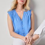 Woman wearing a blue sleeveless top and white pants sitting on a white surface.