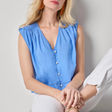 Woman wearing a blue sleeveless top and white pants sitting on a white surface.