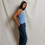 Woman wearing a blue top and dark jeans against a plain white background