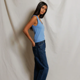 Woman wearing a blue top and dark jeans against a plain white background